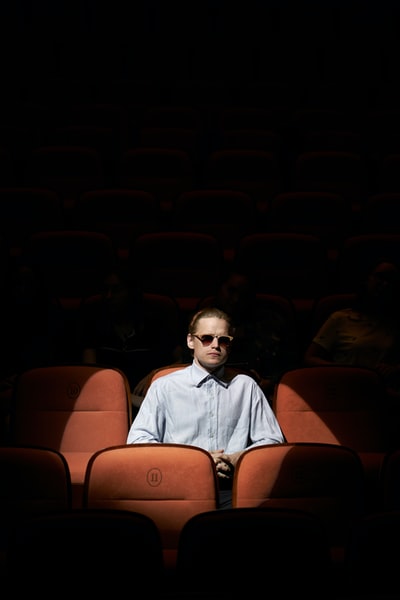 一个穿着蓝色衬衫，戴着墨镜的男人坐在棕色的椅子上